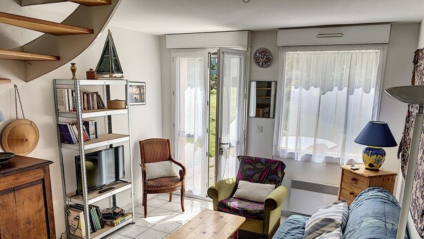 Un salon chaleureux avec une table basse en bois, un canapé, une bibliothèque, un fauteuil et une fenêtre avec des rideaux.