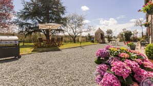 Un patio de grava con mobiliario exterior, una parrilla y un edificio de piedra.