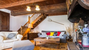 Una sala acogedora con una escalera de madera, chimenea y un sofá con cojines coloridos.