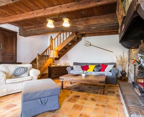 A cozy living room with a wooden staircase, a fireplace, and a sofa with colorful cushions.