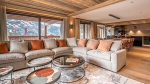 A modern living room with a sectional sofa, round coffee tables, and a view of a mountain landscape through large windows.