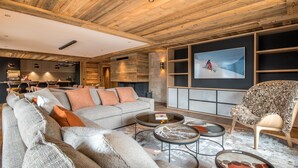 A modern living room with a wooden ceiling, a large sofa, a coffee table, and a television mounted on the wall.