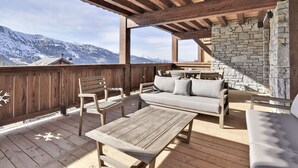 A wooden deck with a stone wall, wooden furniture, and a view of snow-capped mountains.