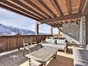 Una terraza de madera con un muro de piedra, mobiliario de madera y vistas a montañas nevadas.