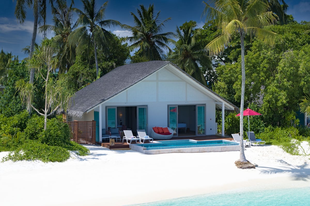 A beachfront villa with a pool, lounge chairs, and a view of the ocean.