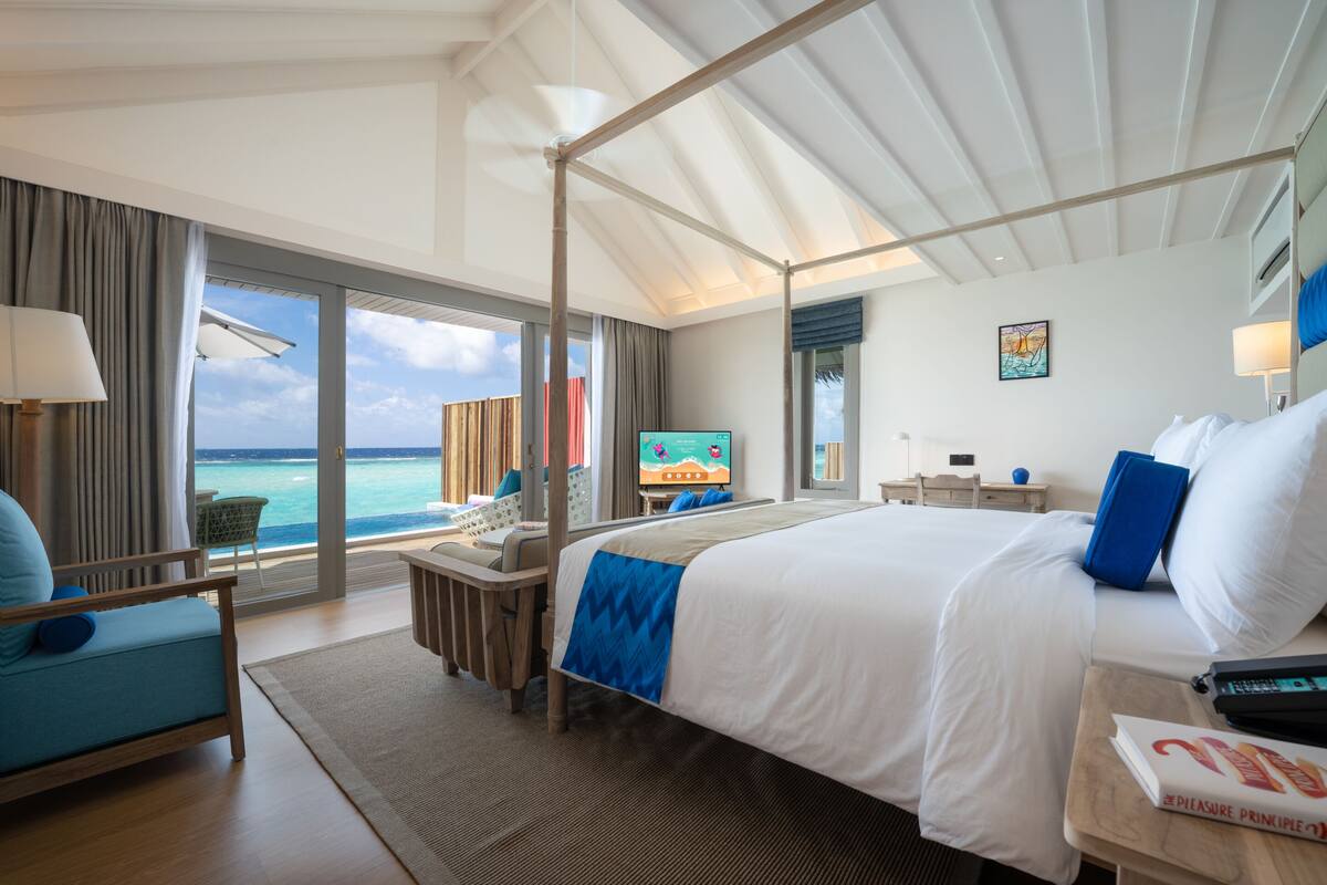 A hotel room with a large bed, a TV, a desk, and a view of the ocean.