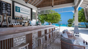Un bar frente a la playa con mostrador de piedra, taburetes y mobiliario de mimbre.
