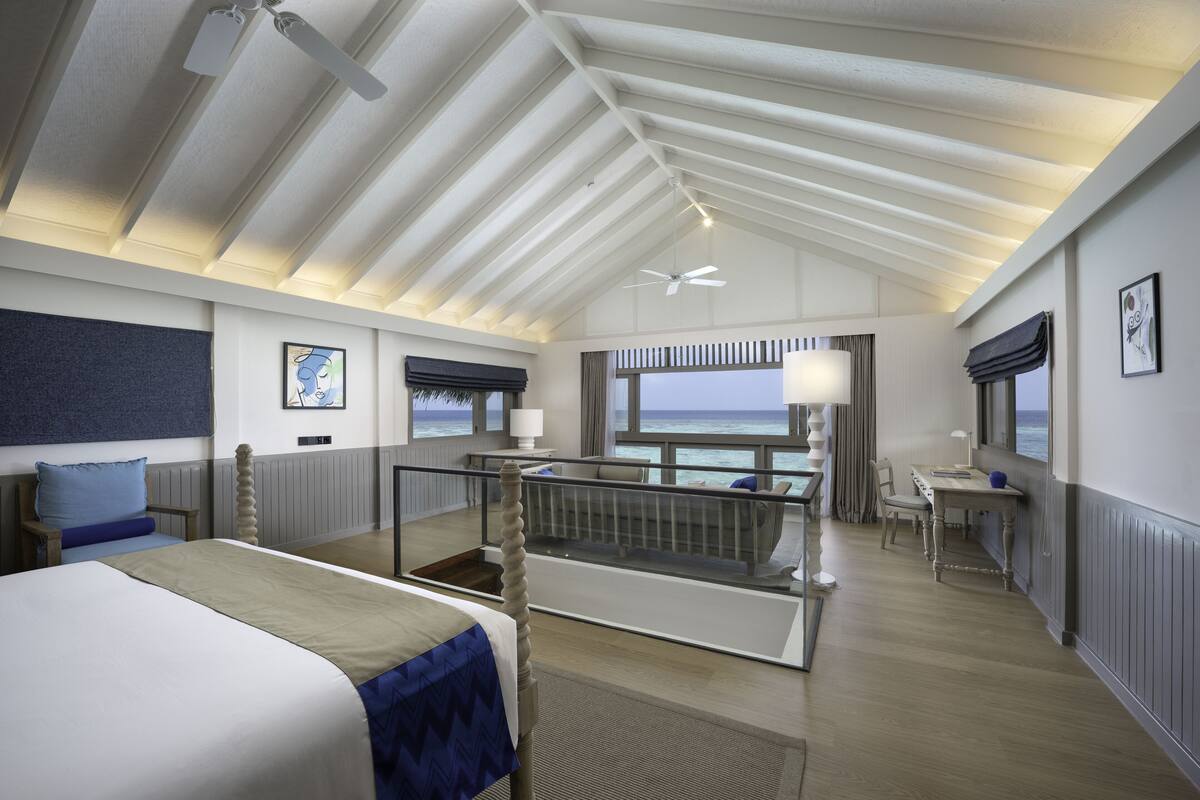 A modern hotel room with a balcony, a bed, a desk, and a view of the sea.