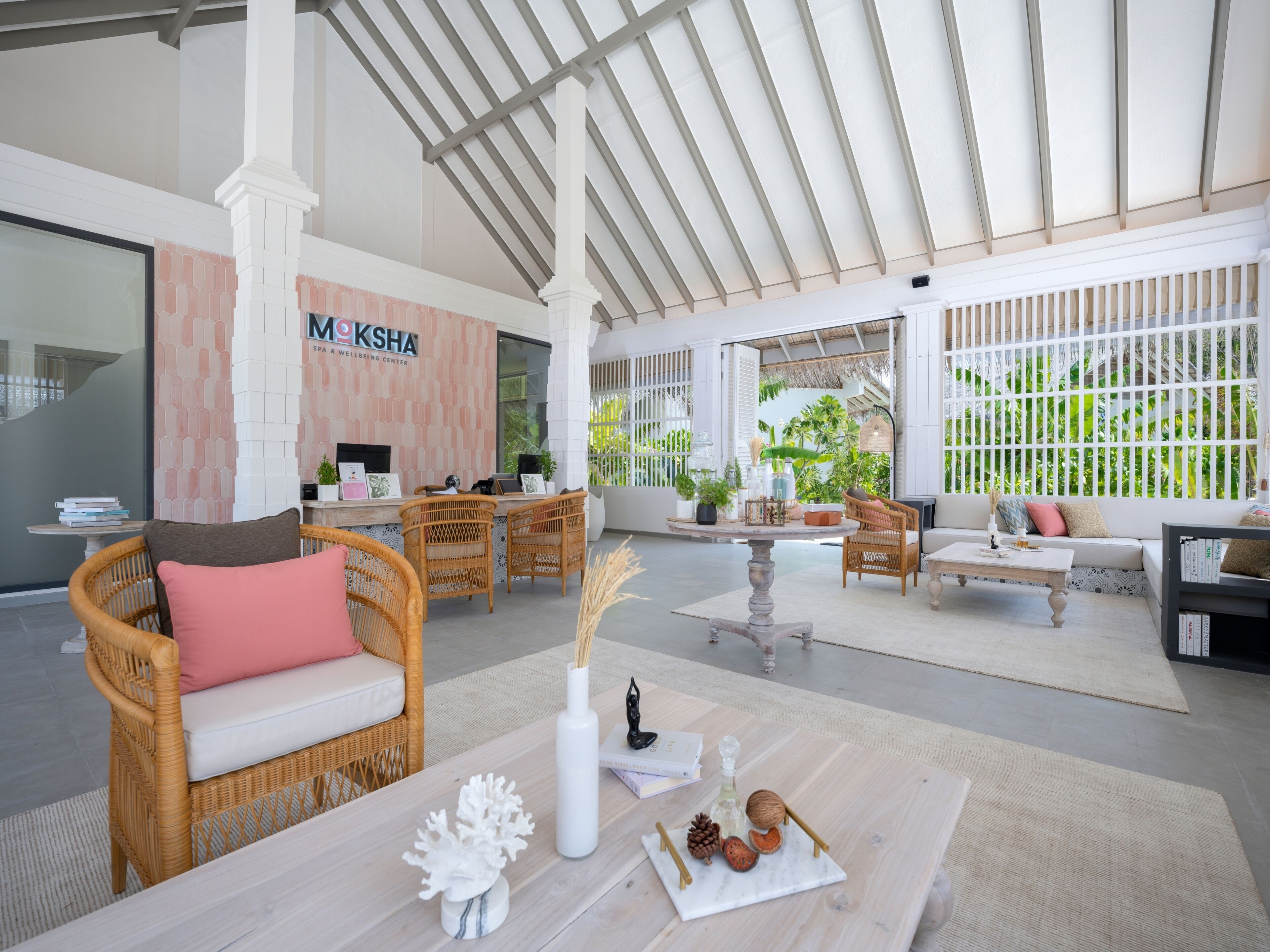 A spacious, well-lit indoor area with wicker furniture, a reception desk, and a view of lush greenery outside.