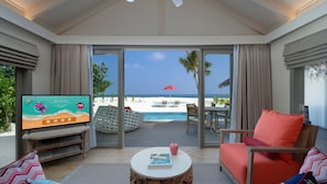 A modern living room with a television, a round wooden coffee table, and a view of the beach and ocean through large glass doors. - Cora Cora Maldives-Premium All-Inclusive (Maamigili Island)