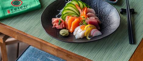 Une assiette noire sur laquelle est présentée une sélection de sushis, accompagnée de baguettes et d’une serviette verte.
