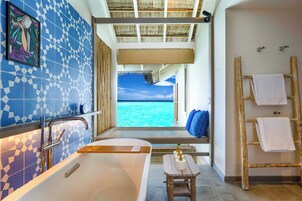 A bathroom with a bathtub, a wooden stool, a towel rack, and a view of the ocean.