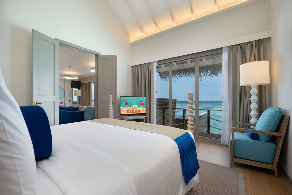A hotel room with a large bed, a TV, a chair, and a view of the ocean.