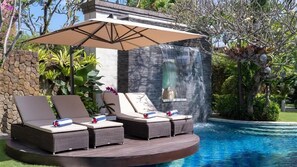 Un área junto a la piscina con un jacuzzi, sillas de descanso y una cascada.