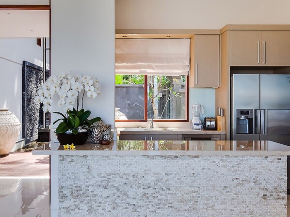 Una cocina moderna con encimera de mármol, electrodomésticos de acero inoxidable y vistas al exterior.