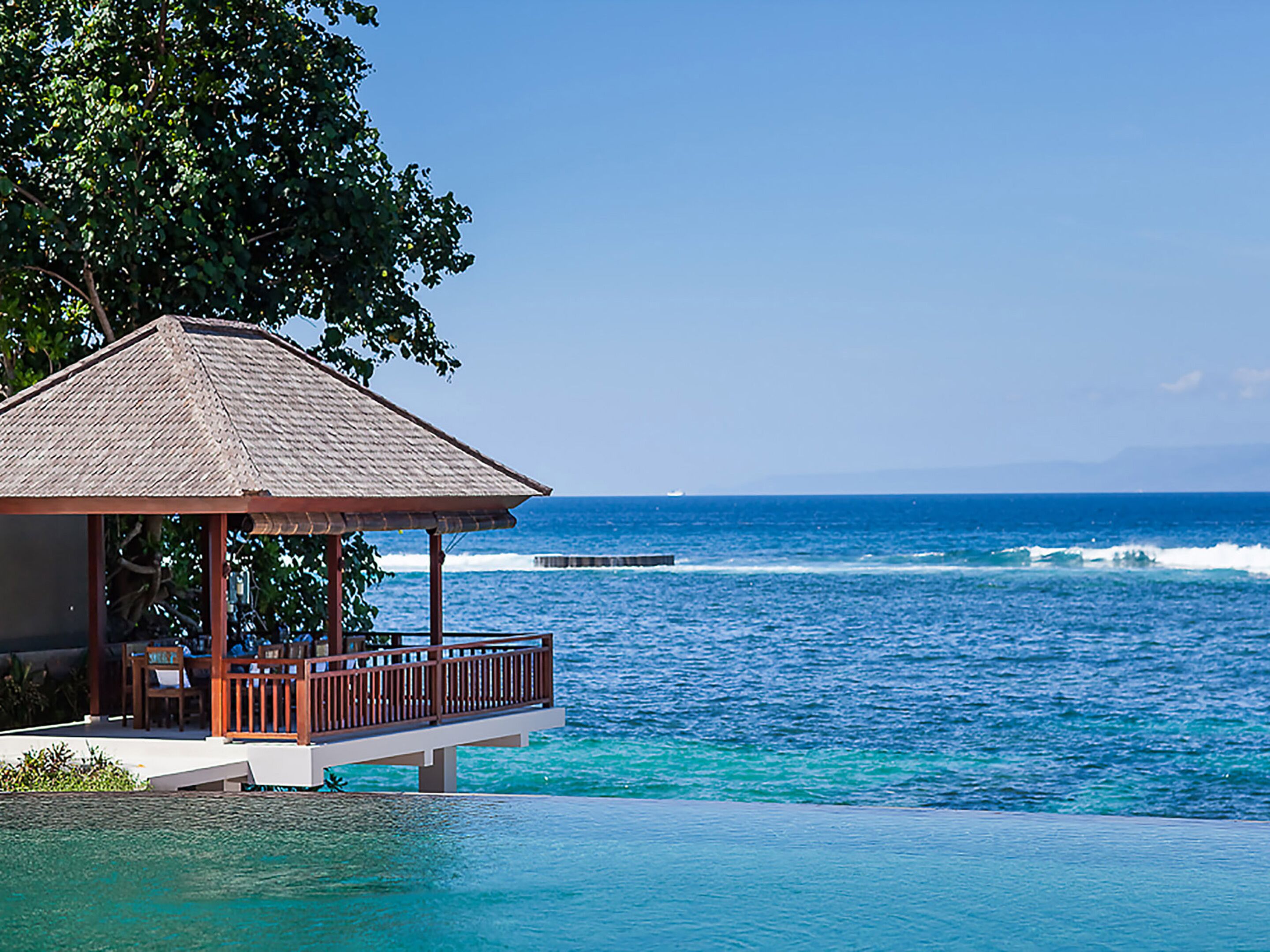 A beachfront infinity pool with a wooden deck and lounge chairs, overlooking the ocean.