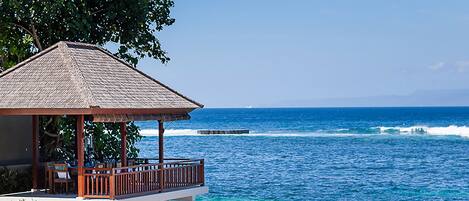 A beachfront infinity pool with a wooden deck and lounge chairs, overlooking the ocean.