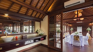 A spacious room with a wooden ceiling, a large window, and a long table set for a formal event. - Villa San (Ubud)