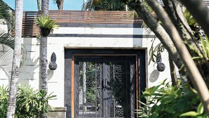 A modern building entrance with a decorative metal gate, steps leading up to the door, and surrounding greenery. - Villa San (Ubud)