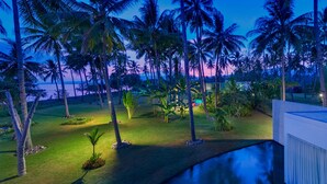 Paesaggio tropicale con palme, una piscina e vista sull'oceano al tramonto.