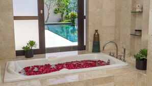 Un baño con una bañera llena de pétalos de rosa, una ducha con cerramiento de vidrio y vista a una piscina.