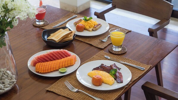 A breakfast table with plates of food, a glass of orange juice, and a bottle of water. - Villa Adenium by Elite Havens (Jimbaran)