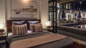 Un dormitorio con cama, almohadas, una mesita de noche, una lámpara y un cuadro en la pared.
