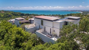 Una villa moderna con varios niveles, rodeada de exuberante vegetación y con vistas al mar.