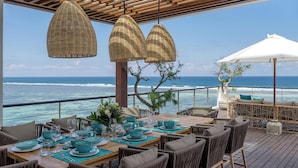 A dining area with a view of the ocean, wicker pendant lights, and a white umbrella. - Grand Cliff Nusa Dua (Nusa Dua)