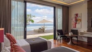 A modern hotel room with a large window overlooking the ocean, a bed, a seating area with a table and chairs, and a small desk with a chair. - Grand Cliff Nusa Dua (Nusa Dua)