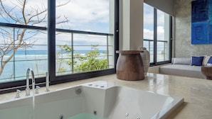 A modern bathroom with a large bathtub, a view of the ocean, and a seating area with a sofa and decorative vases. - Grand Cliff Nusa Dua (Nusa Dua)