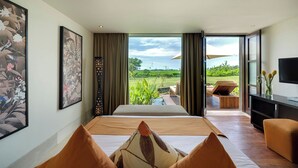 A bedroom with a large bed, a TV, and a view of a garden. - Mandalay Villas (Munggu)