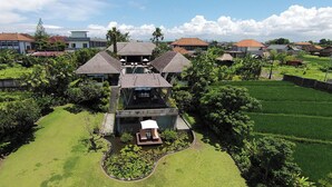A large, multi-story building with a central courtyard, surrounded by lush greenery and adjacent rice paddies. - Mandalay Villas (Munggu)