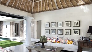 A spacious living area with a white sofa, a coffee table with books, and a wall decorated with framed artworks. - Villa Adasa (Seminyak)