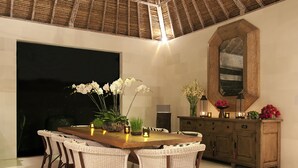 A dining area with a large wooden table surrounded by wicker chairs, a wooden cabinet with decorative items, and a large mirror on the wall. - Villa Adasa (Seminyak)