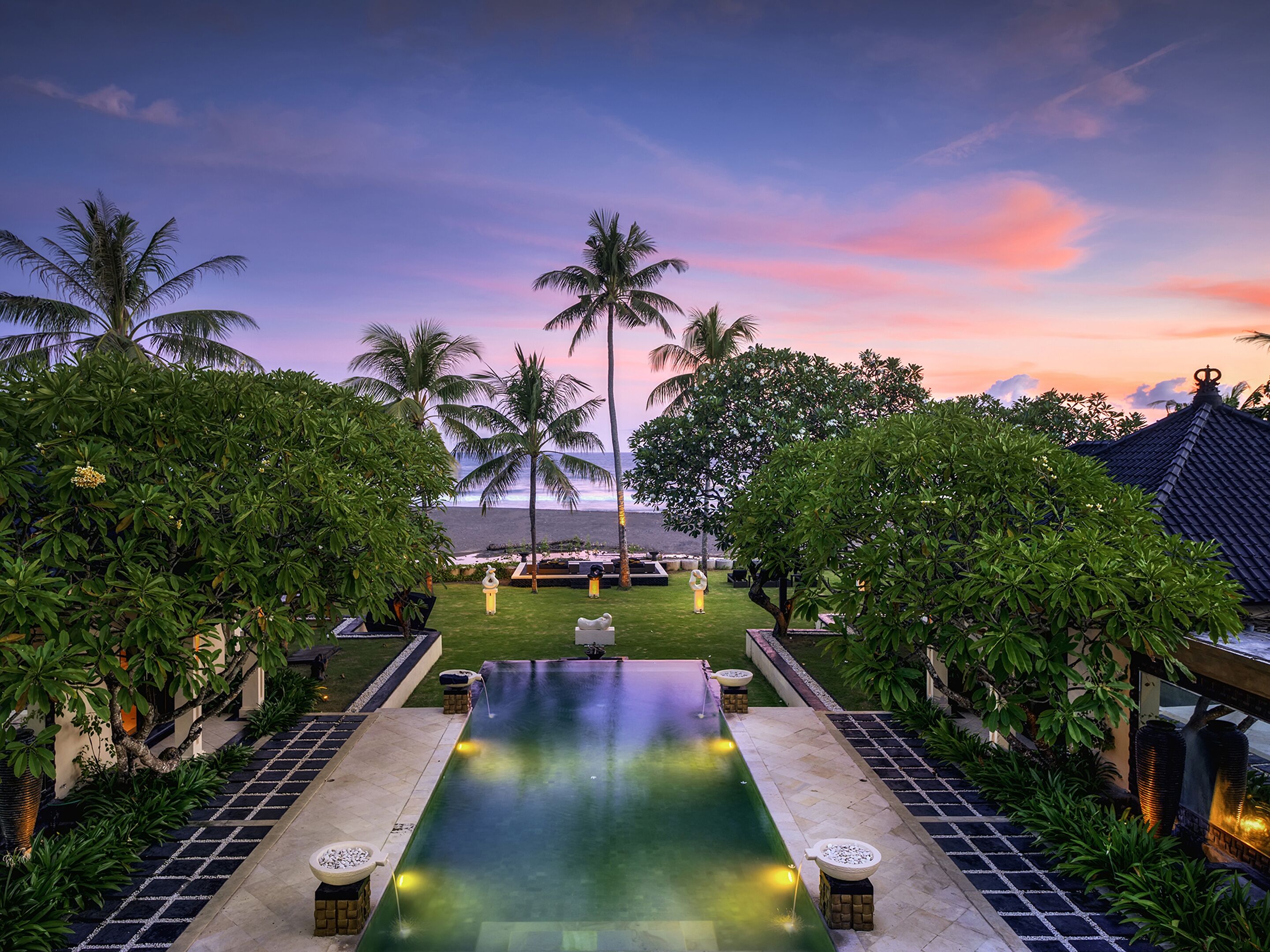 A pool with a view of the ocean, surrounded by palm trees and a traditional building.