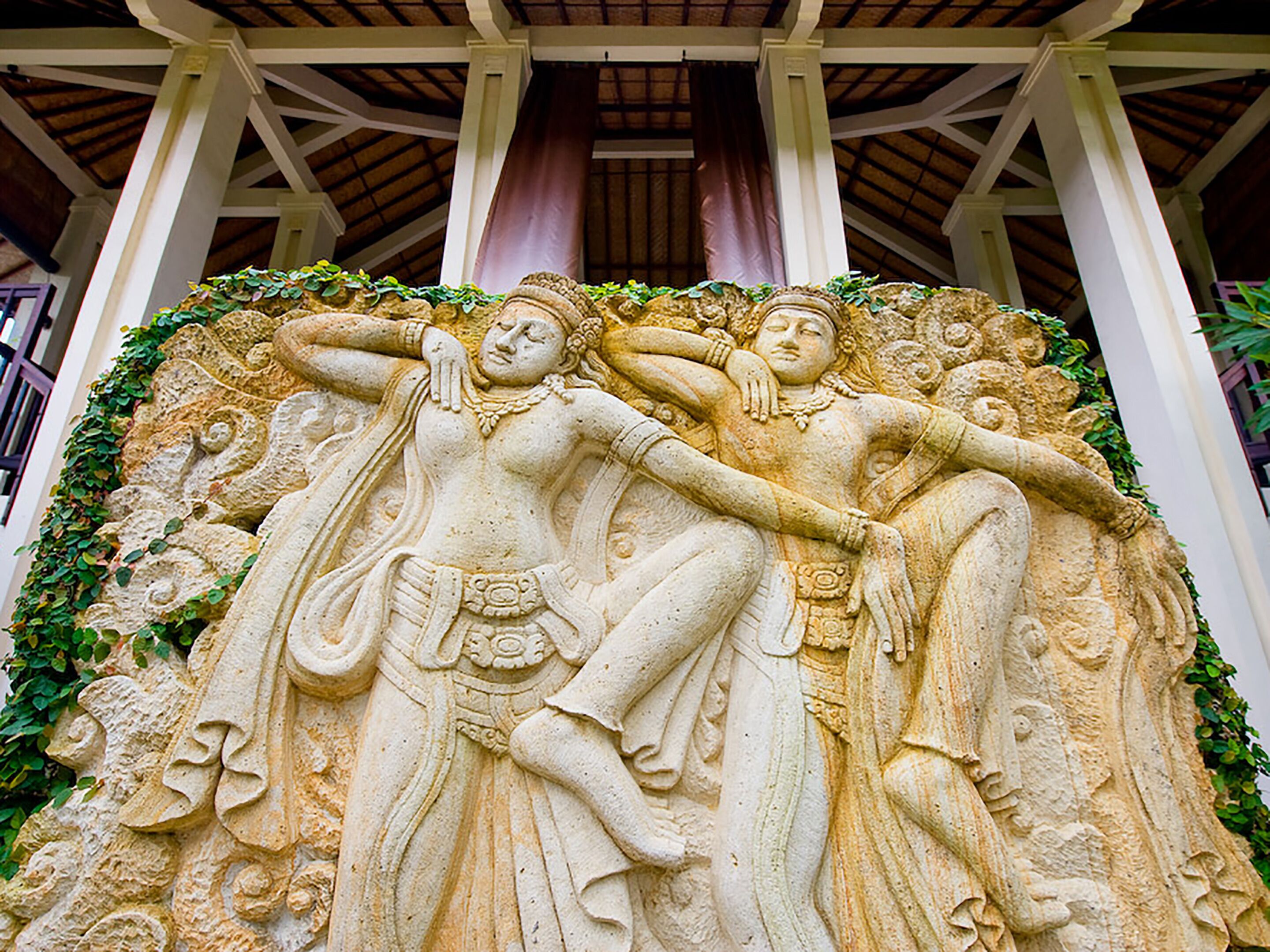 Escultura de piedra que representa dos figuras en una pose tradicional, rodeada de vegetación.