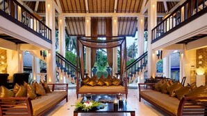 A spacious lobby with a central seating area, a staircase, and large windows offering a view of greenery. - The Ylang Ylang (Blahbatuh)