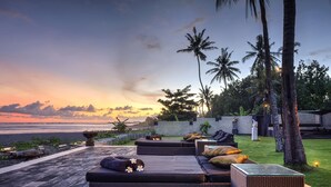 A serene outdoor seating area with wicker furniture and a view of the ocean at sunset. - The Ylang Ylang (Blahbatuh)