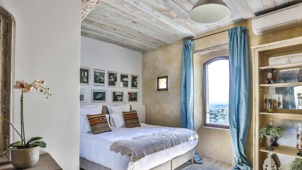 A bedroom with a bed, a window with curtains, a wall with framed pictures, and a shelf with decorative items. - Apartement Like a Local Gordes (Gordes)