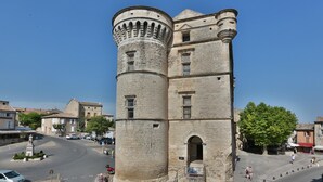 A historic stone tower with a central arched entrance, surrounded by a cobblestone square with pedestrians and parked cars. - Apartement Like a Local Gordes (Gordes)