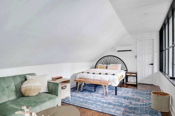 Une chambre à coucher avec un lit, un canapé vert, une petite table, un banc et une grande fenêtre.