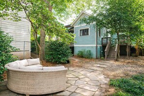 A backyard with a stone patio, a wicker sofa, and a blue house with a staircase.