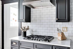 A modern kitchen with a gas stove, black cabinets, and a white tiled backsplash. - Aix-EN-Atlanta (Atlanta)