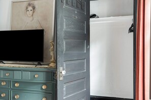A room with a television on a dresser, a gray door, and a white wall.