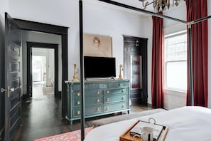 Ein Schlafzimmer mit einem Bett, einem Schminktisch, einem Fernseher und einem Fenster mit Vorhängen.