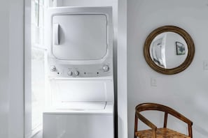 Ein Zimmer mit einer weißen Waschmaschine, einem Holzstuhl und einem Spiegel an der Wand.