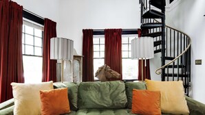 En grøn sofa med orange og hvide puder, en skulptur af et hestehoved og en sort spiraltrappe.