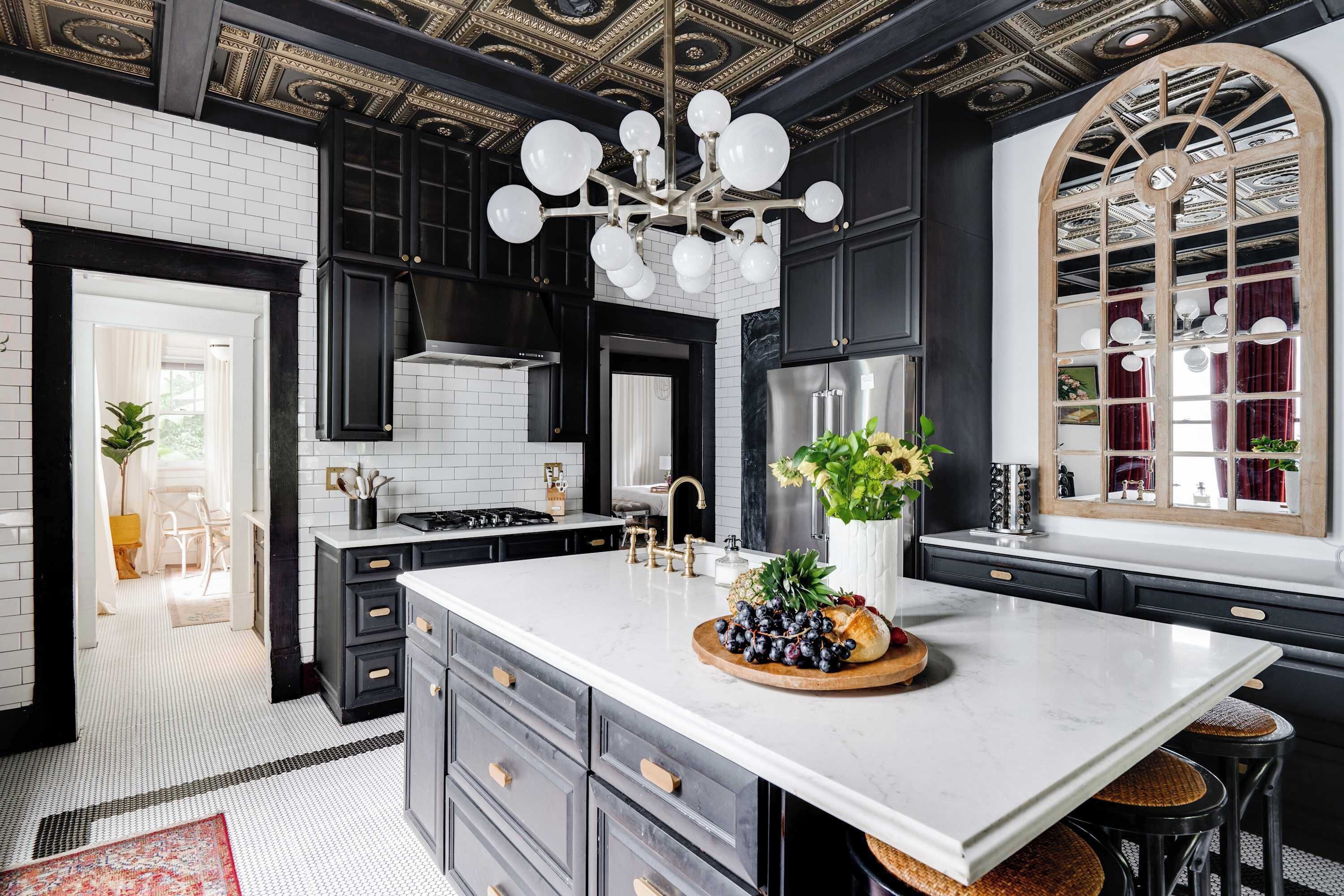 A modern kitchen with a large island, black cabinetry, white marble countertops, and a decorative ceiling.