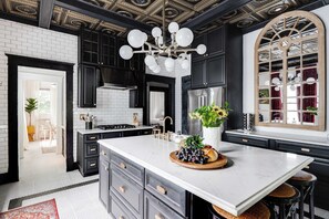 Une cuisine moderne dotée d’un grand îlot central, de meubles de rangement noirs, de plans de travail en marbre blanc et d’un plafond décoratif.